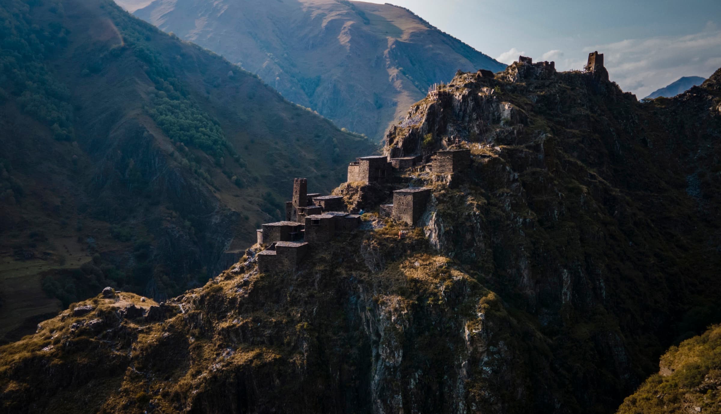 Wide aerial view of Mutso's stone towers and fortified dwellings stretched along a narrow, steep ridge, with layered Khevsureti mountains in the background