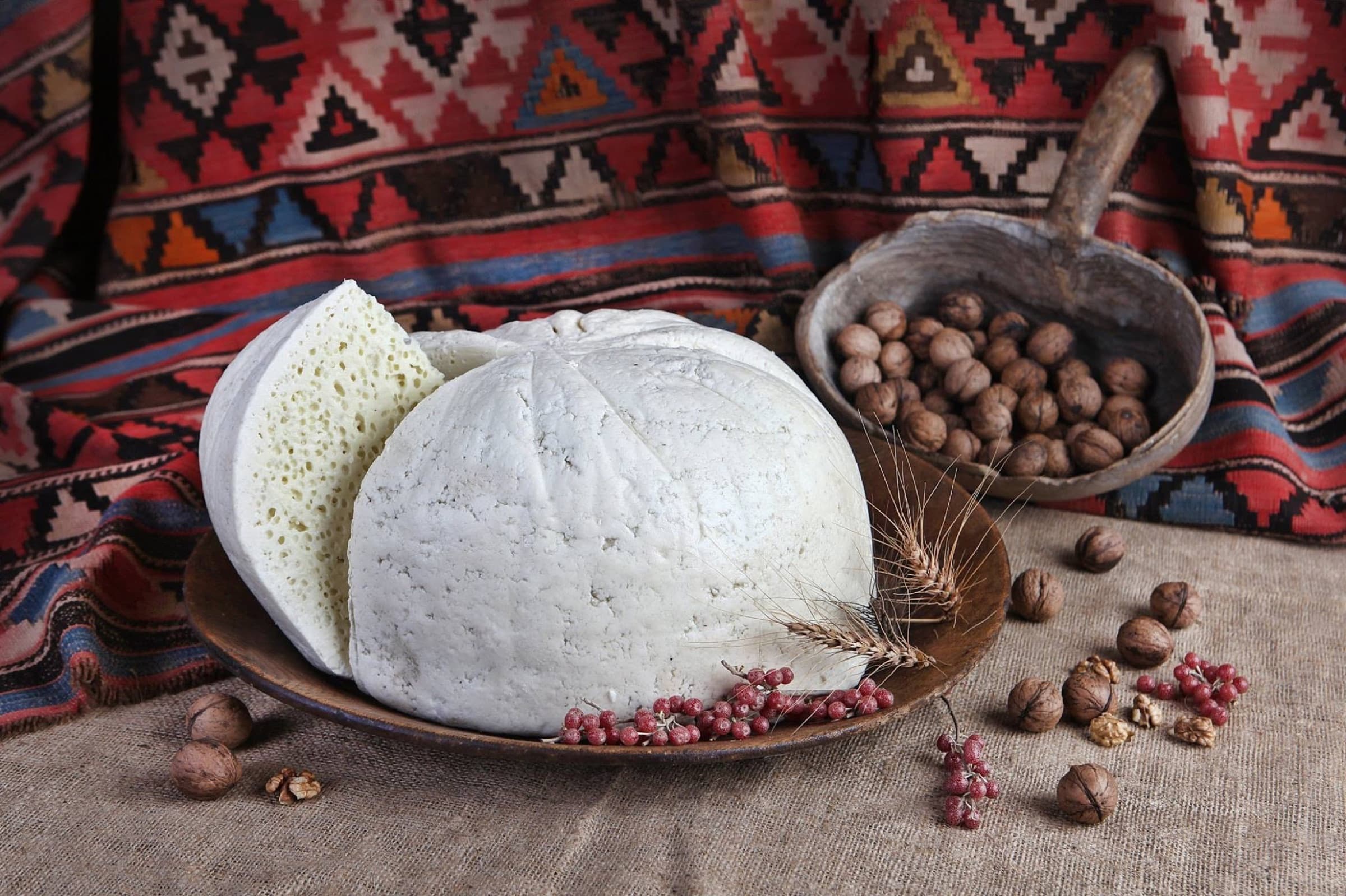Tushetian Guda Cheese - Georgia's Protected Mountain Delicacy Round Tushetian guda cheese sliced open on a wooden plate with walnuts and dried berries