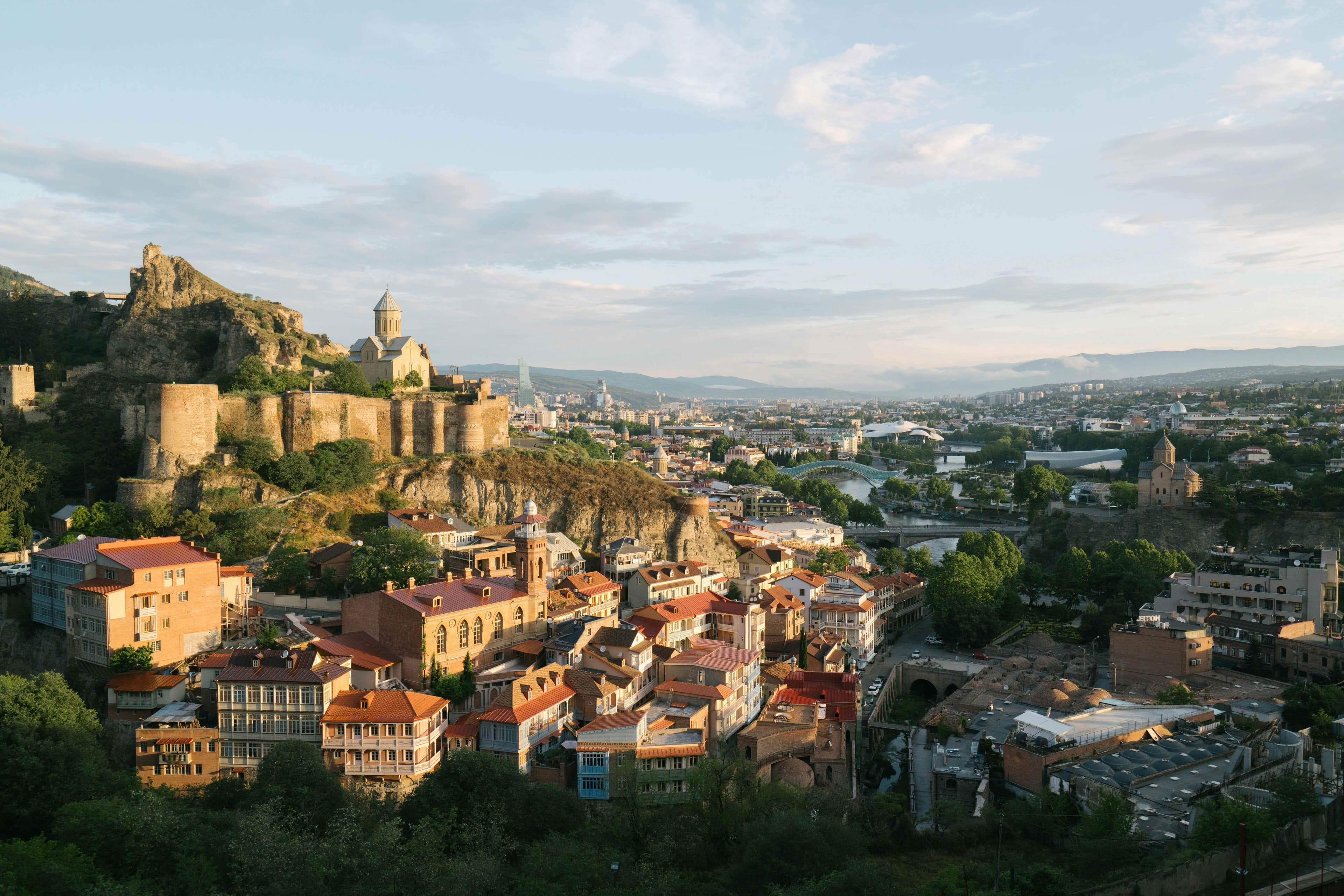 Panoramic view of Tbilisi's Old Town with Narikala Fortress, traditional balconied houses, and Mtkvari River under golden evening light
