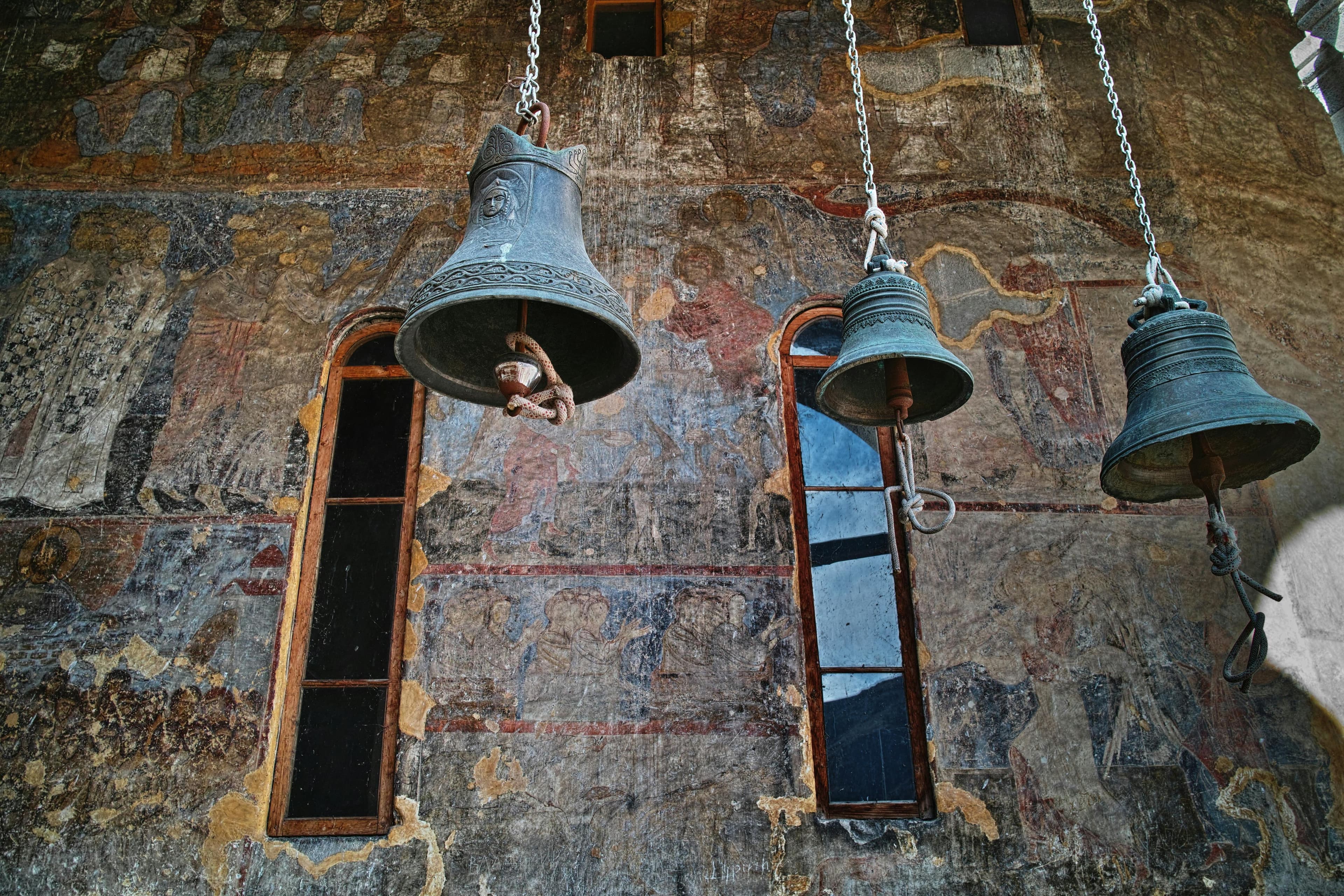 Ancient bronze bells hanging against weathered frescoes at Vardzia cave monastery